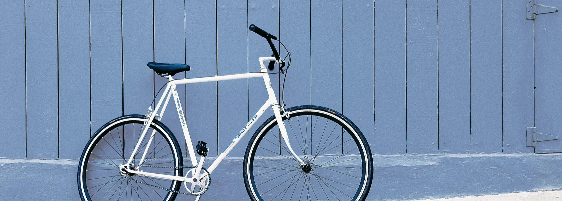 Ein weißes Fahrrad lehnt an einer holzvertäfelten blauen Wand