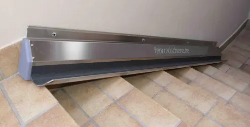Silberne Fahrradschiene aus Metall, angebracht an einer Fliesentreppe neben einer Wand