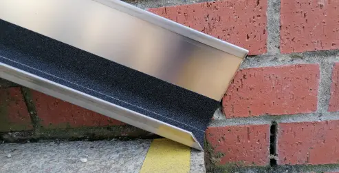 Nahaufnahme einer Fahrradschiene aus Metall mit rutschfester Oberfläche, montiert an einer Backsteinmauer