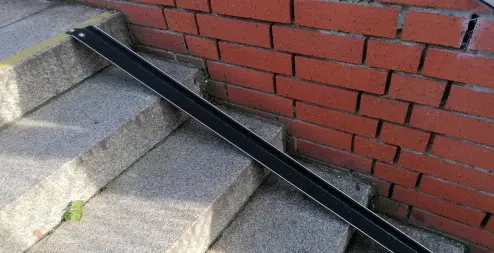 Schwarze Fahrradschiene aus Metall, installiert an einer Steintreppe neben einer roten Backsteinwand