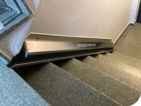 Bild einer Fahrradschiene aus Edelstahl die an einer Treppe in einem Flur verlegt ist
