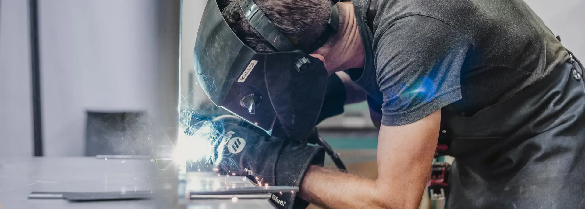 Handwerker mit Schweißhelm beim Schweißen von Metall an einem Arbeitstisch